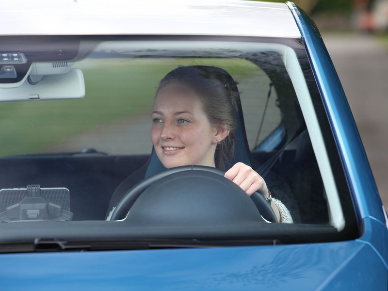 Eine junge Frau fährt stolz mit ihrem Auto.